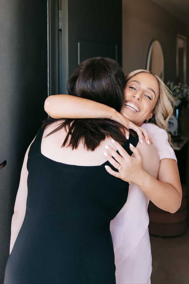 Two women hugging in a doorway with a neutral background