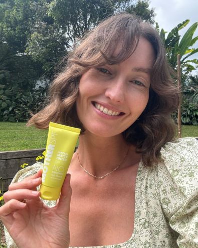 Smiling woman holding a mother-mousse-spf50 outdoors in natural light.