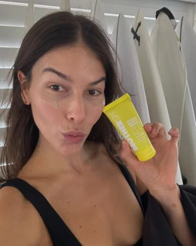 Woman holding a yellow sunscreen tube indoors.