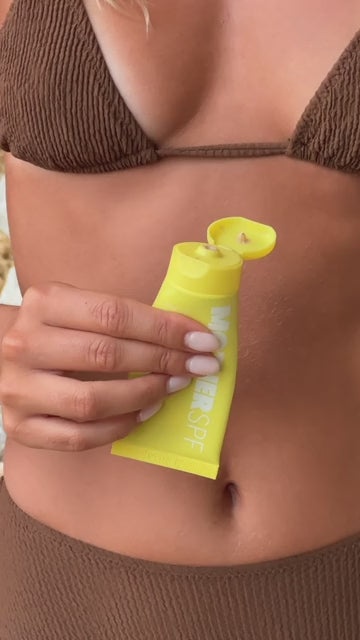 Close-up of person squeezing sunscreen product from a yellow tube.